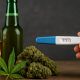 A photograph showing a glass of alcohol and a beer bottle on the left, cannabis buds and a leaf in the center, and a hand holding a positive pregnancy test on the right, all arranged on a wooden surface with a dark background.