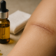 A cinematic widescreen photo showing a glass dropper bottle of golden hemp seed oil next to folded gauze, with a close-up of a healed scar on skin, symbolizing natural wound-healing research.