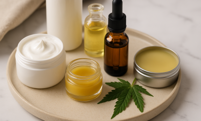 Assorted cannabis-infused topicals, including cream, balm, oil bottles, and a cannabis leaf, arranged neatly on a beige tray for a wellness-themed setting.
