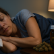 A woman sleeps peacefully in bed at night, with a bedside table holding an amber prescription bottle and dried cannabis buds under the soft glow of a lamp.