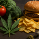 A photorealistic widescreen image showing a cannabis leaf placed between fresh whole foods like avocado, tomatoes, spinach, and broccoli on the left, and ultra-processed foods like chips, cheeseburger, and cheese curls on the right, symbolizing the contrast between healthy nutrition and processed diets in relation to cannabis use.