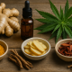 A rustic wooden table displaying turmeric powder, fresh ginger, sliced ginger, dried danshen roots, thunder god vine pieces, and cannabis leaves arranged with an amber dropper bottle, symbolizing natural remedies for rheumatoid arthritis.