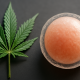A photorealistic widescreen image showing a cannabis leaf beside a human egg cell on a dark surface, symbolizing research on cannabis and female fertility.