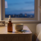 An amber CBD oil tincture bottle and a ceramic cup on a wooden nightstand at dusk, featuring a digital clock showing 9:30 PM and a blurred window view of the blue hour.