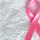 Pink breast cancer awareness ribbon on a white textured background symbolizing hope and support.